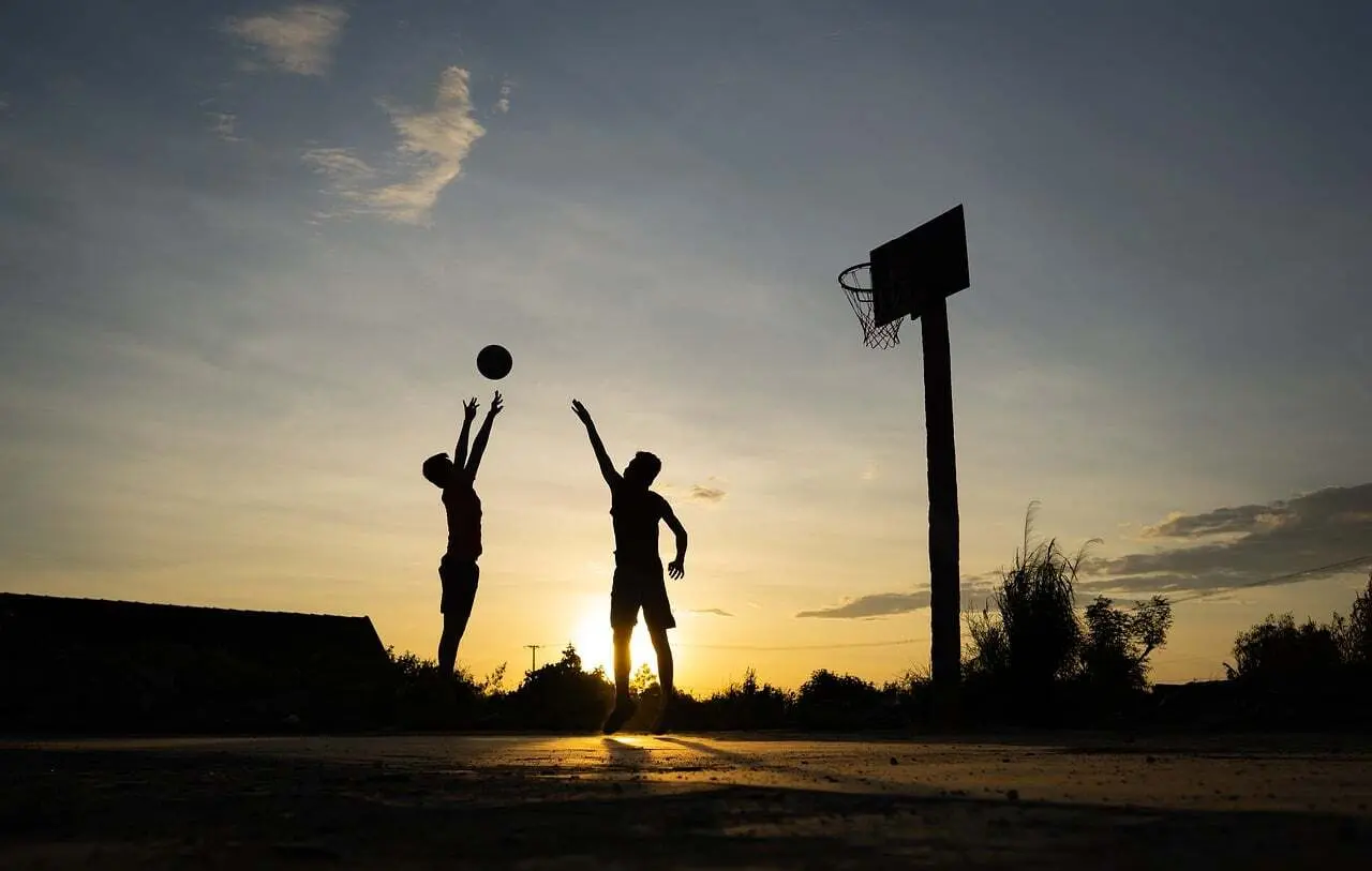 Silhuetter spiller basketball ved solnedgang